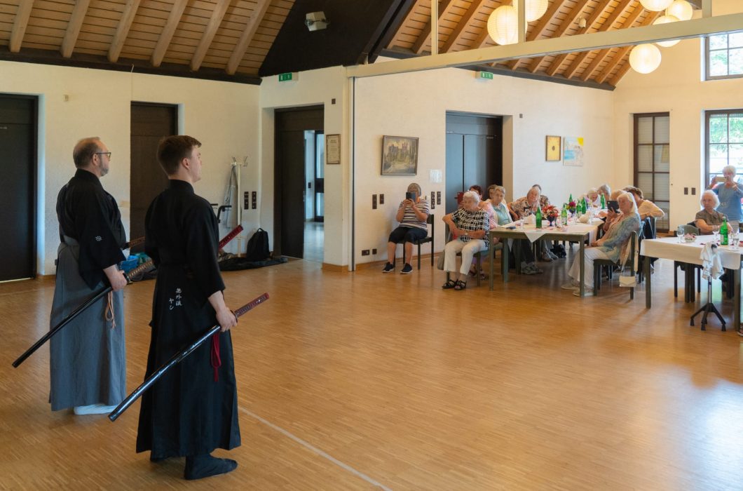 a man in a black robe holding a sword in a room with people